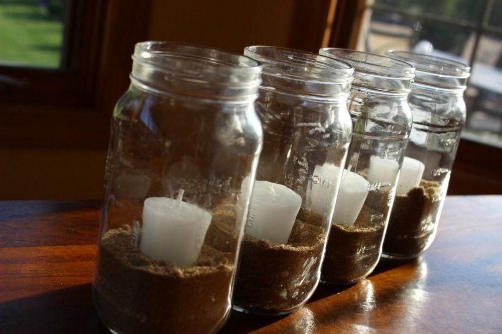 mason jar centerpieces with 4 jars containing sand and small white candles.