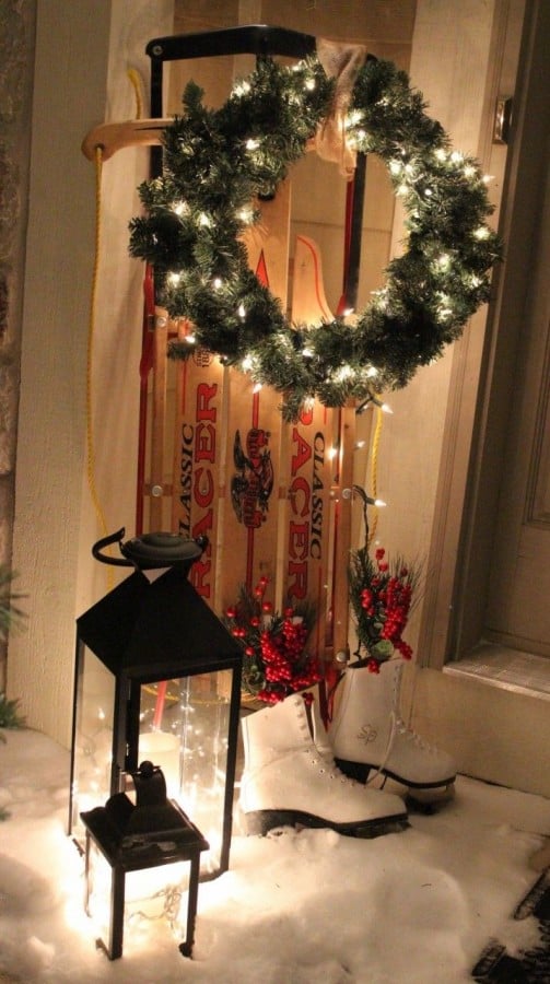 Christmas wreath with white lights hanging on a vintage sled with skates placed near the sled