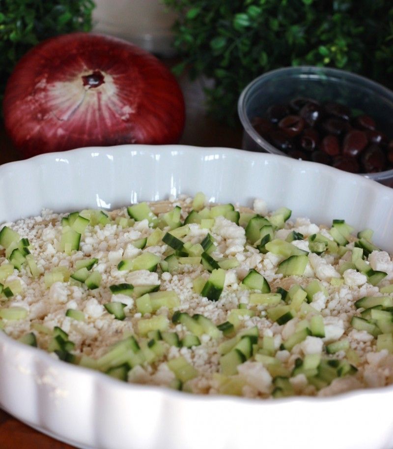 Cheese spread, hummus and chopped cucumbers are the beginning of assembling this Greek layer dip.