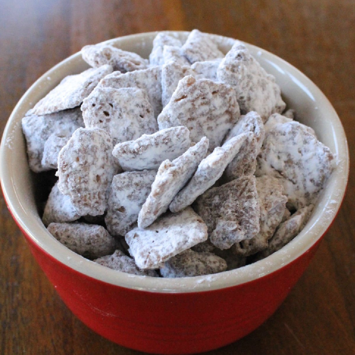 Confectioner coated cereal treat known as puppy chow in a small red bowl.