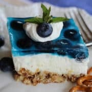 a piece of blueberry pretzel dessert with a base layer of pretzel crumbs, then a light cloud layer of cream cheese and whipped cream and on top blueberries in blueberry jello.