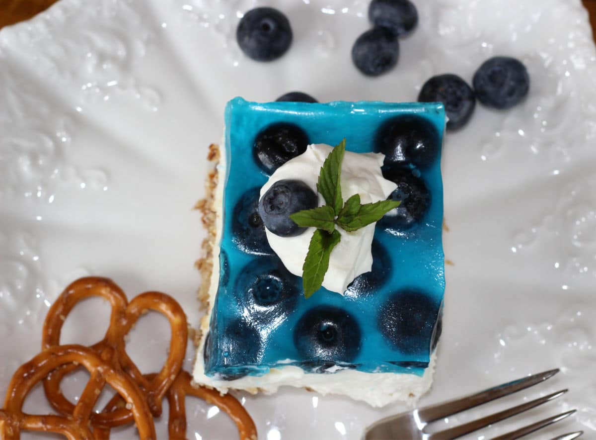 blueberry pretzel salad dessert on a white plate with pretzels and blueberries as garnish.
