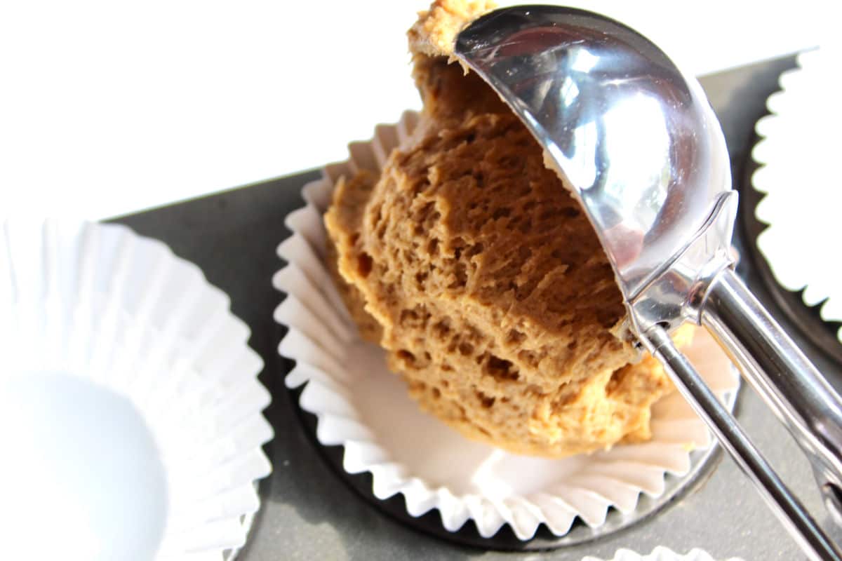 Scoop of pumpkin muffin batter being put into a muffin liner.