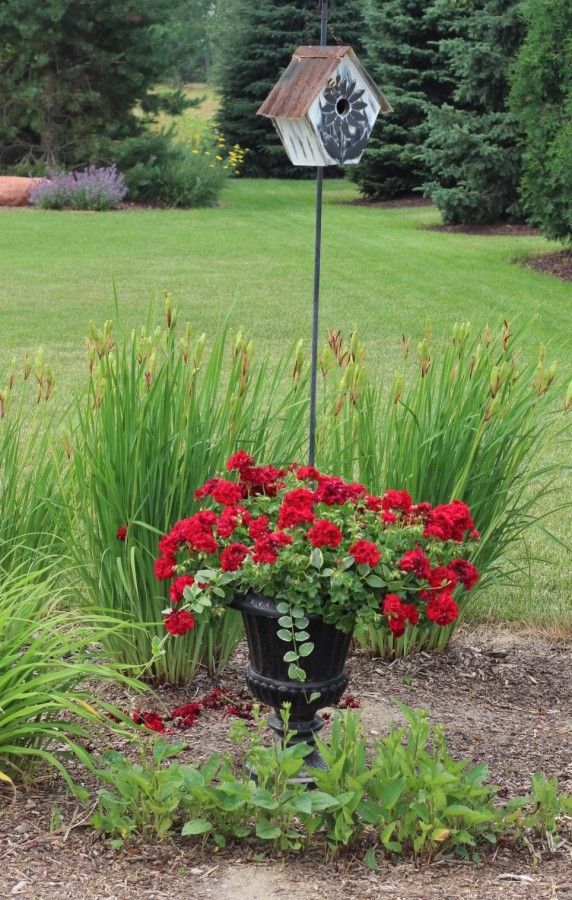 Red geraniums in a planter with a birdhouse on a tall stake.