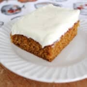 Piece of pumpkin bar on a white plate with a tray of pumpkin bars in the background.