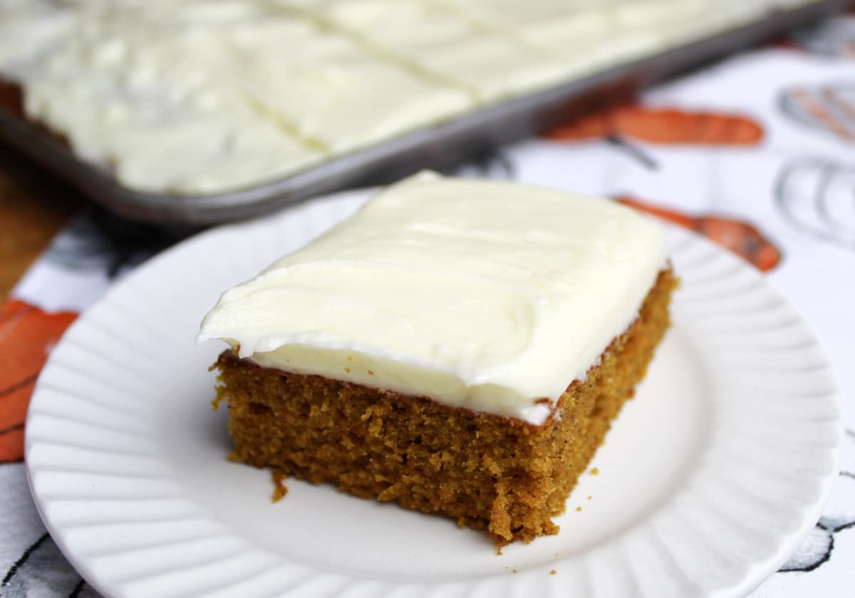 a piece of pumpkin bar with cream cheese frosting with a sheet of cut bars in the background.