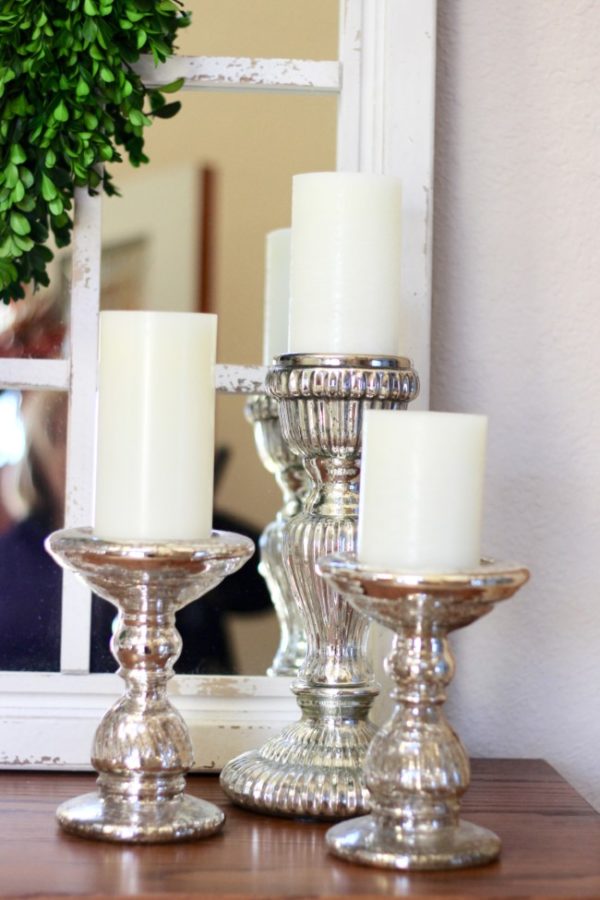 white candles on mercury glass candle holders sitting in front of a chippy white farmhouse mirror