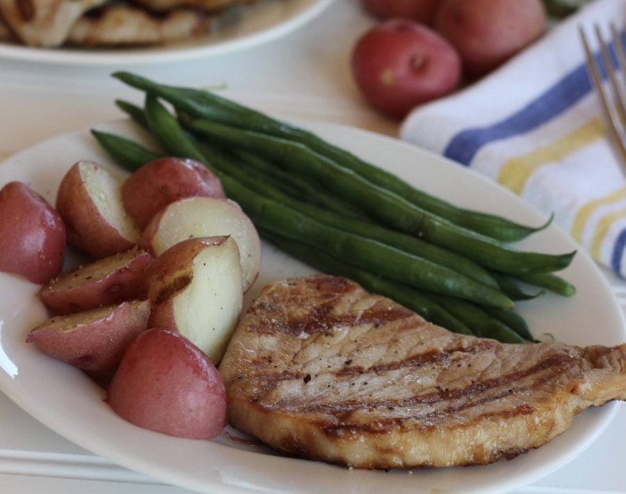 pork chop with sides of green beans and red potatos on a white plate