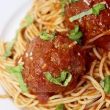 Meatballs covered in spagetti sauce, sitting on spagetti noodles.