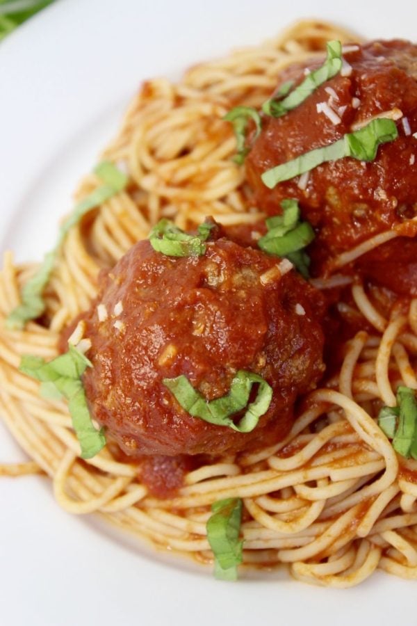 Meatballs covered in spagetti sauce, sitting on spagetti noodles.