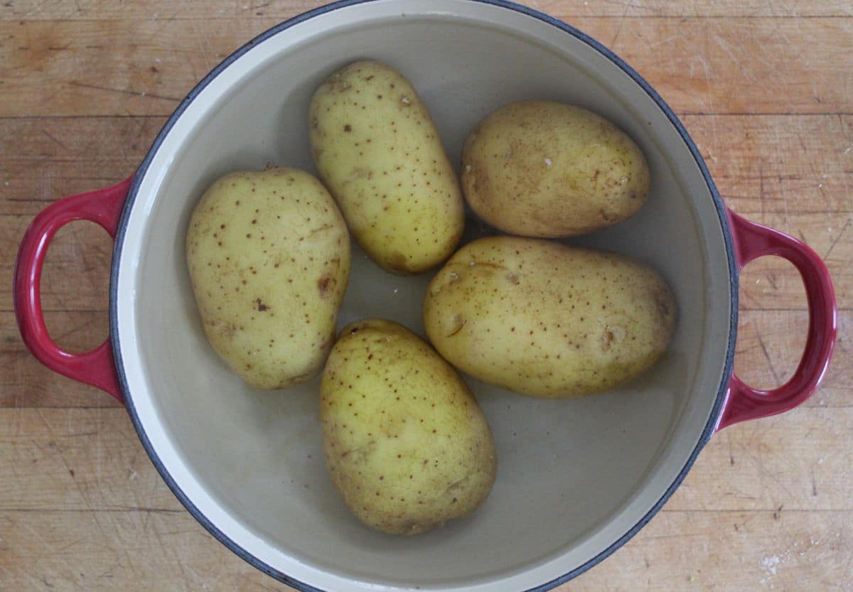 five whole potatoes covered with water in a pot
