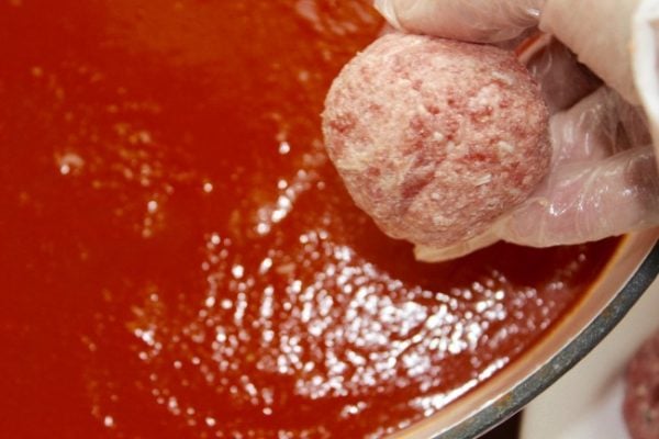 A uncooked meatball being placed into spagetti sauce.