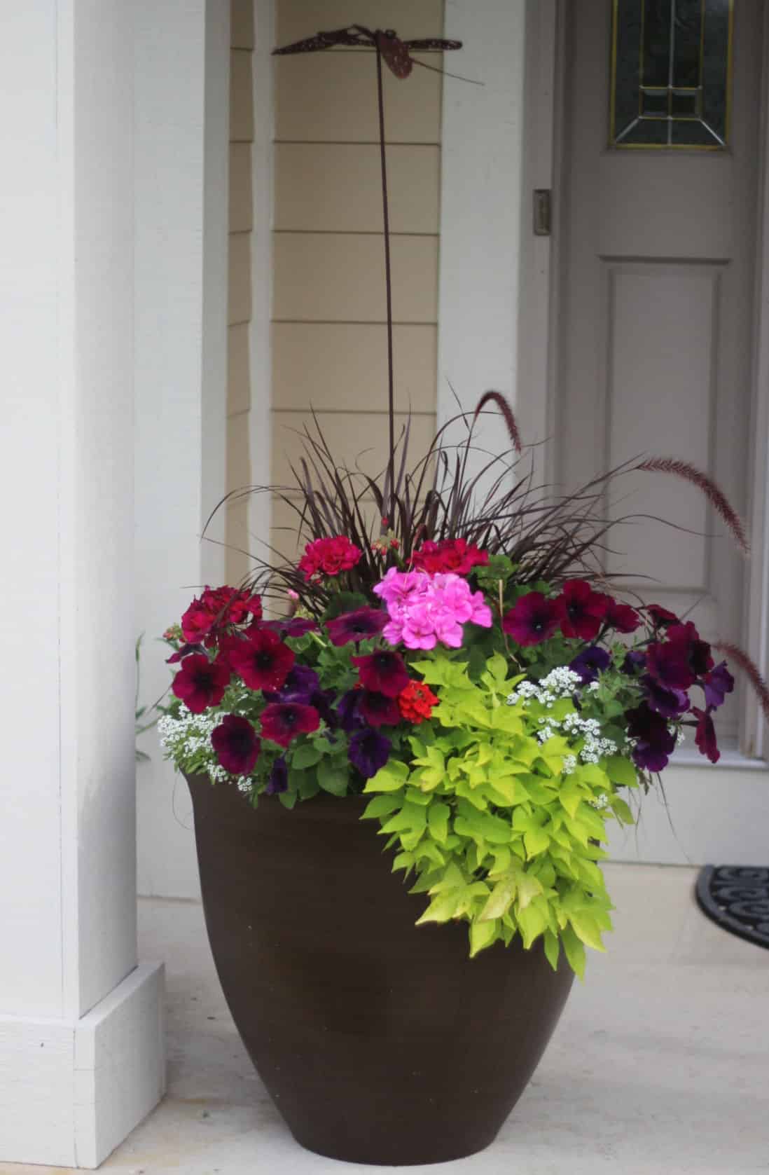Tall planter with pink geraniums, purple petunias and lime sweet potato vine.  The planter has a tall rust colored decorative stake in it.