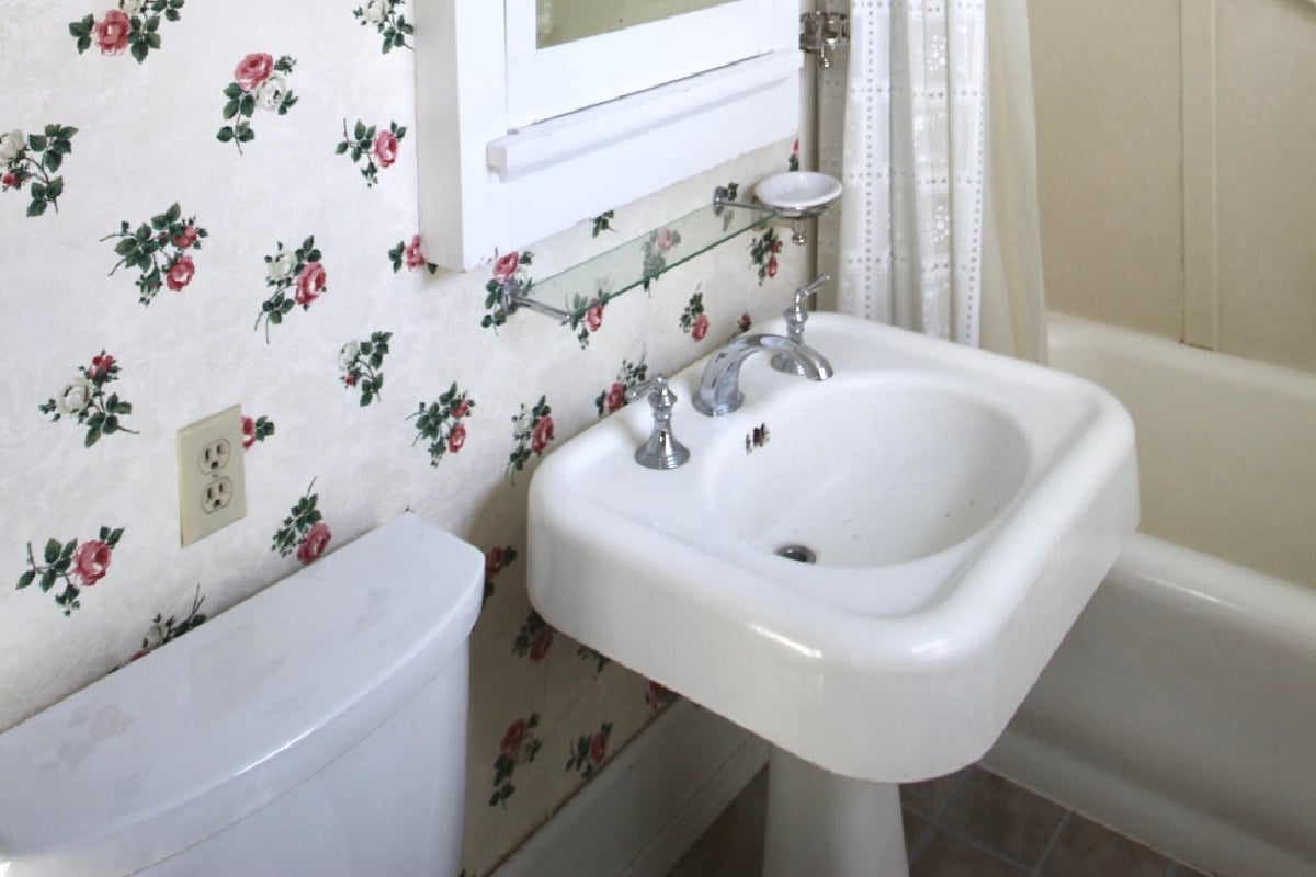 A view of the original main bathroom.  The original rose flowered wallpaper can be seen behind the vintage sink.