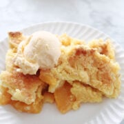 a serving of peach cobbler with a crispy topping and peaches showing. Served on a white plate.