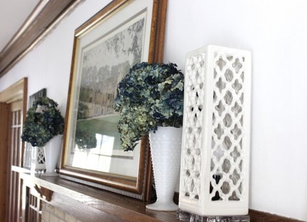 A very simple mantle in my vintage 1920's home. A print of an old English manor house, blue dried hydrangeas and some lighting on my mantle.