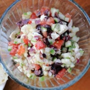 Chopped veggies, olives and feta in a bowl topped with feta and simple dressing.