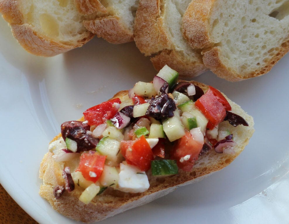 Greek chopped salsa including cucumber, tomato, olives and feta on a slice of bread.