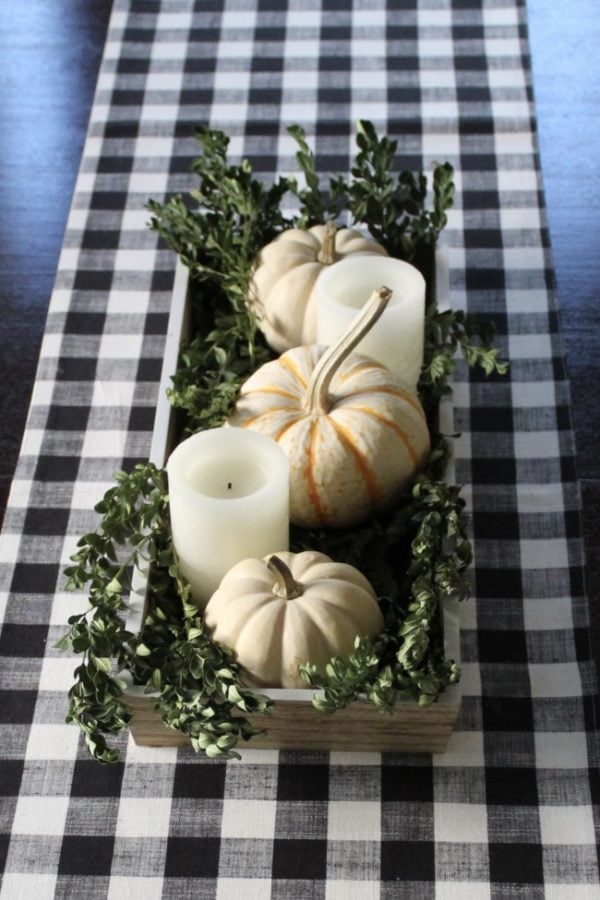 Centerpiece tray with white pumpkins, boxwood branches and white candles.