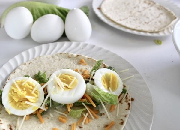 a wrap with caesar salad on a tortilla, with a sprinkling of shredded cheese and sliced hard boiled eggs.