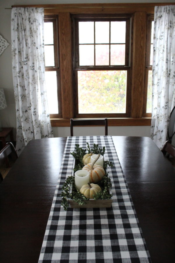 Fall tablescape using small pumpkins in a bread bowl on a buffalo plaid runner