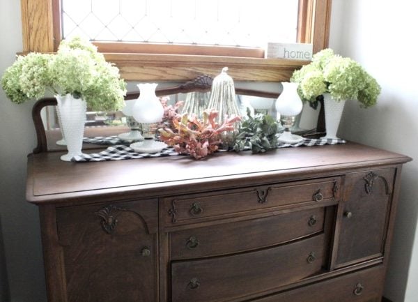 fall decor including dried hydrangeas, milk glass, a mercury glass pumpkin all on a buffalo plaid runner.