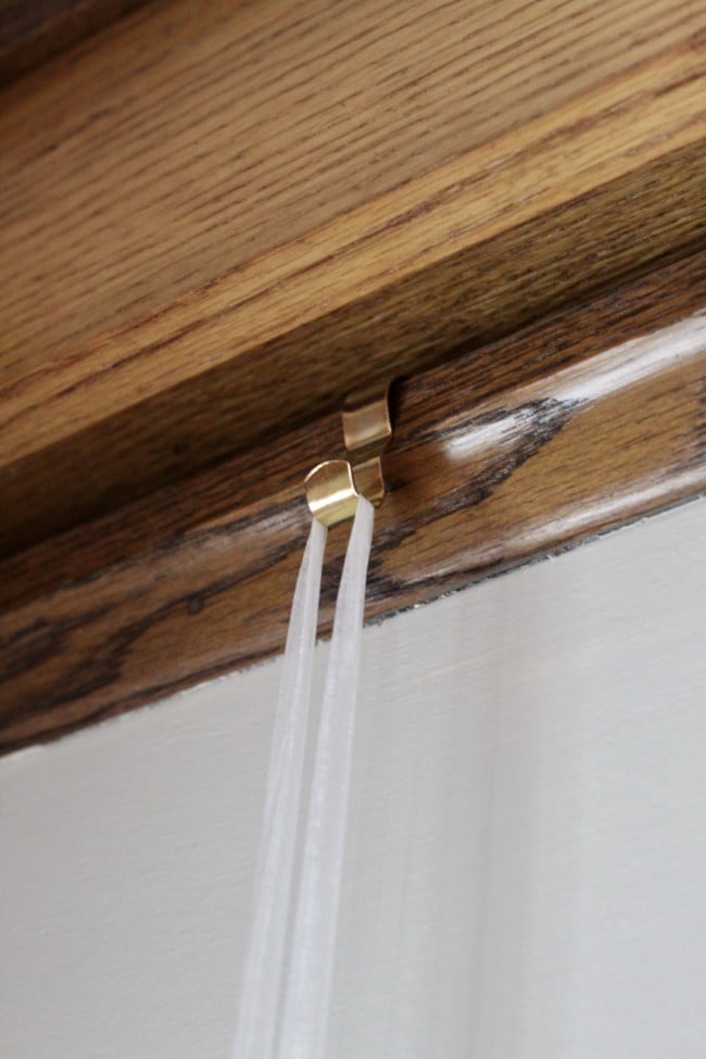 a picture rail hook attached to the picture rail molding with a ribbon attached to it. 