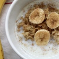 Oatmeal in a white bowl with cinnamon sugar, sliced bananas and milk.