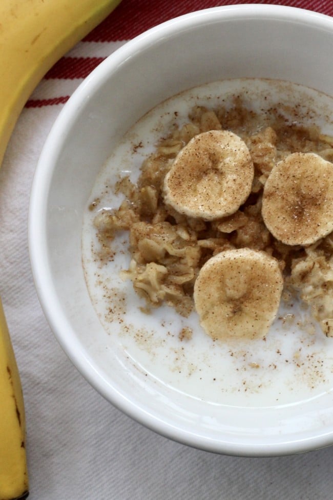 Oatmeal in a white bowl with cinnamon sugar, sliced bananas and milk.