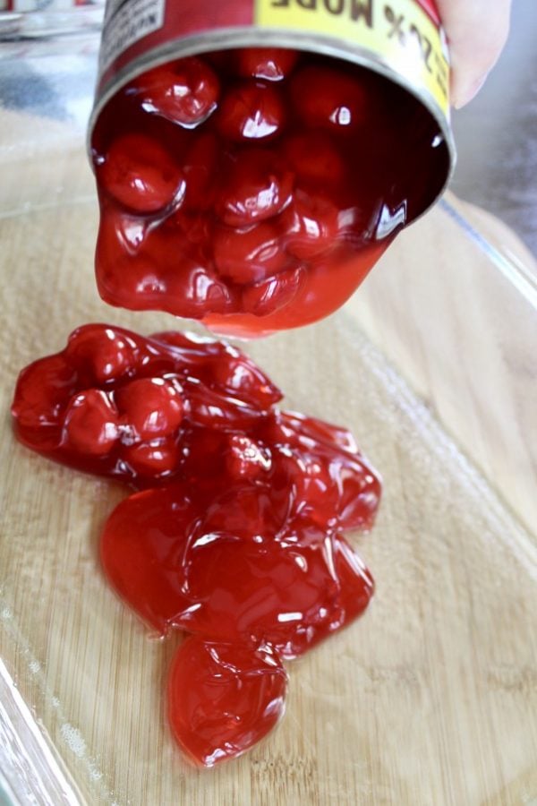 canned cherries being dumped into a casserole dish