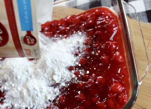 Cake mix being dumped on canned cherries in casserole dish