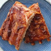 Two servings of rootbeer ribs. Each portion has three ribs and the ribs are covered in barbeque sauce. Served on a blue plate.