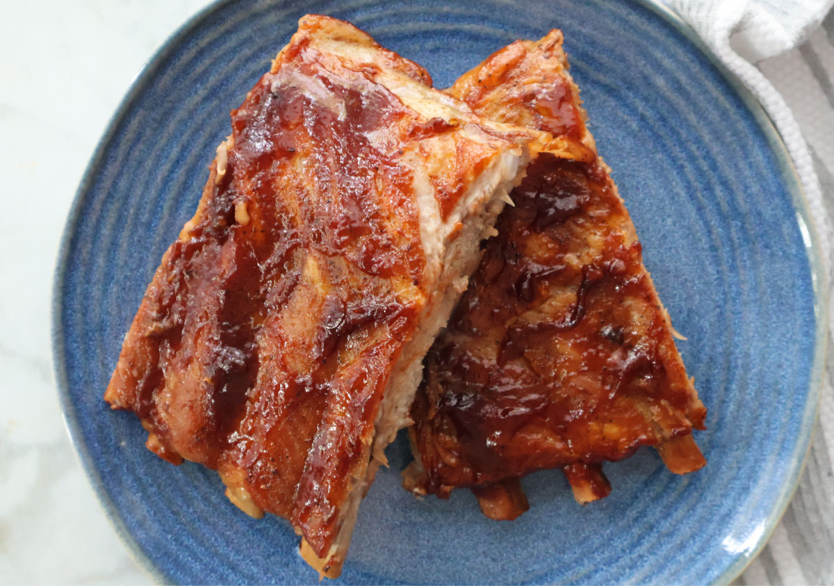 Two servings of rootbeer ribs.  Each portion has three ribs and the ribs are covered in barbeque sauce. Served on a blue plate.