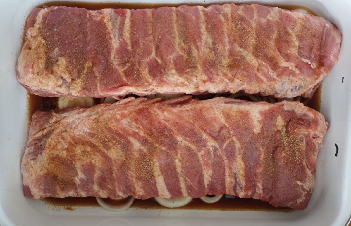 two racks of ribs sitting on top of sliced onions with root beer at the bottom of the roasting pan. 