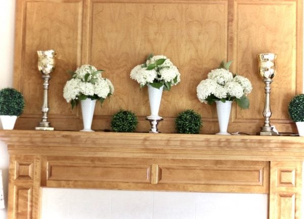 three white milkglass vases full of hydrangeas on a wooden mantle
