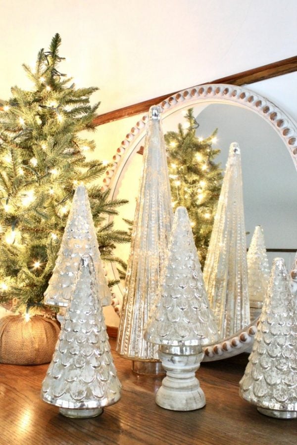 mercury glass trees on white wooden candle holders with a tree with white lights in the background