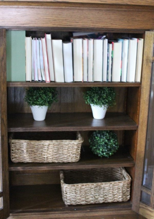 Built-in with open doors that have books, wicker baskets and misc. decor on shelves.