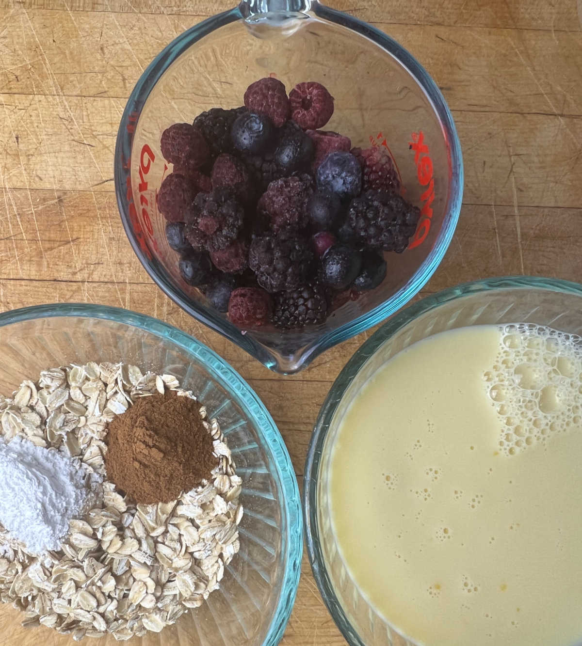 cup of mixed berries, bowl of oatmeal and cinnamon, bowl of mixed milk, eggs and vanilla