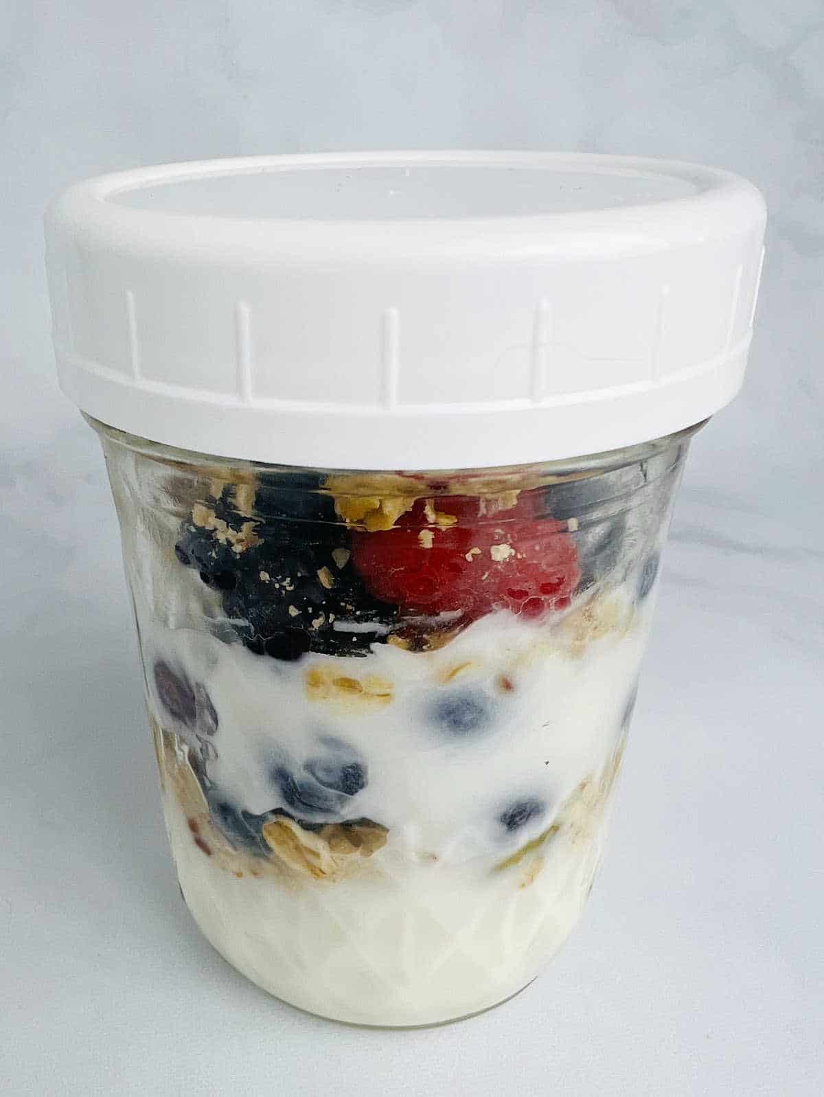 mason jar full of fruit, yogurt and granola with a white lid.