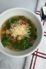 bowl of kale and chickpea soup topped with cheese
