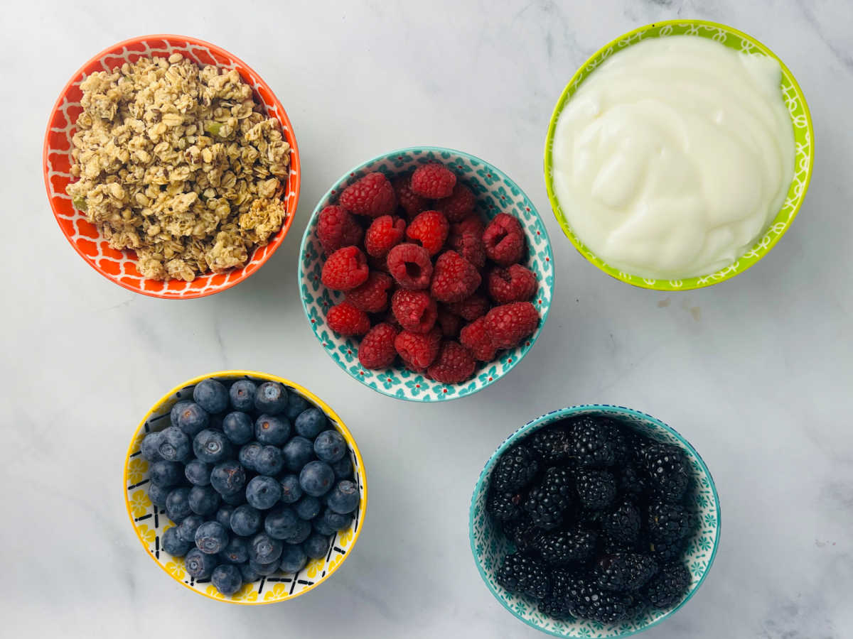 three small bowls of berries, a bowl of yogurt and a bar of granola