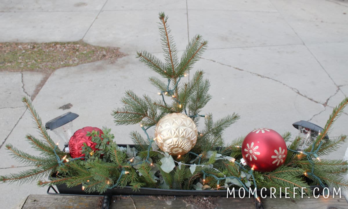 branch that looks like a small tree in a planter with a big gold christmas ornament.