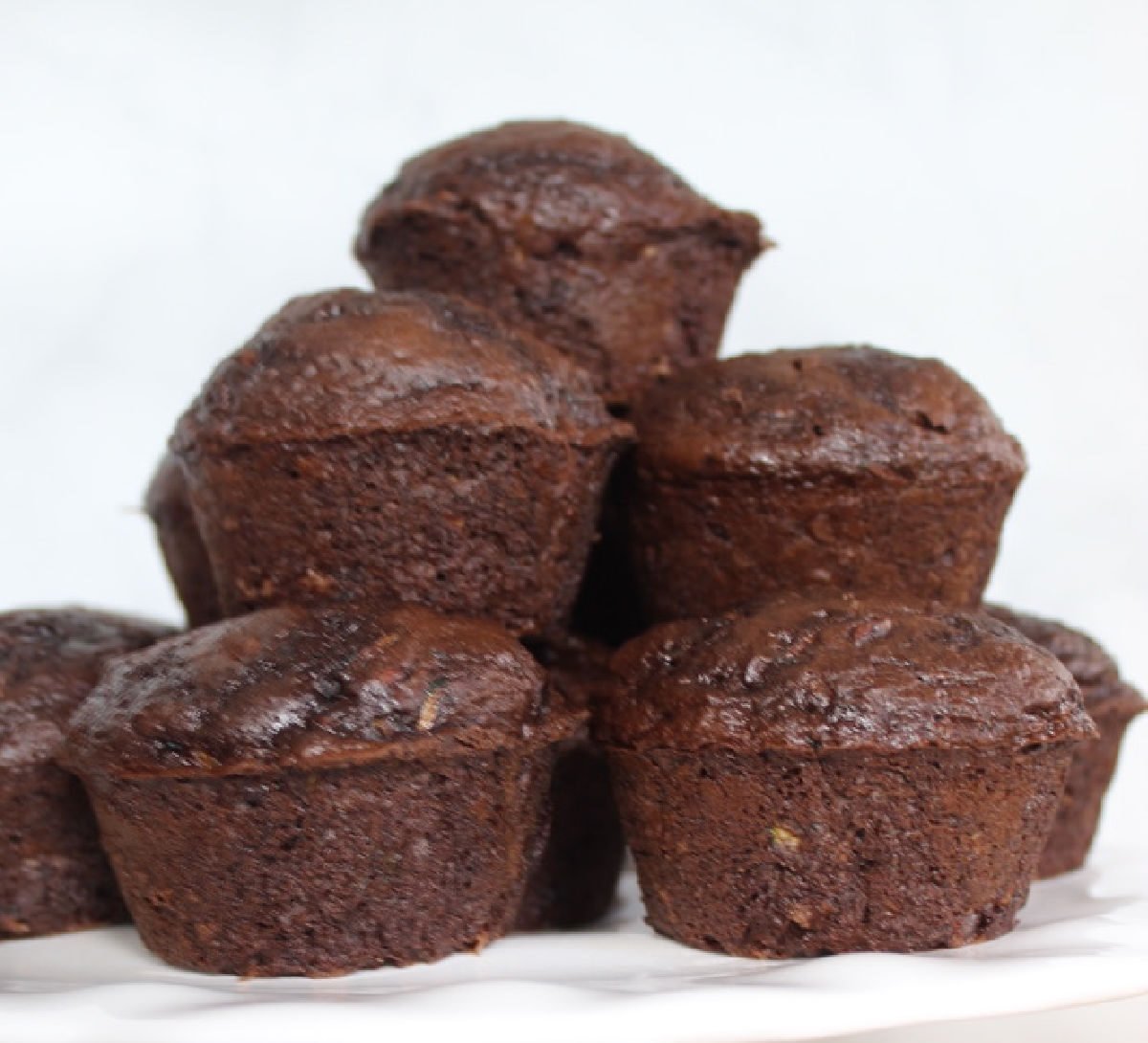 A white cake stand holding stacked chocolate zucchini muffins.