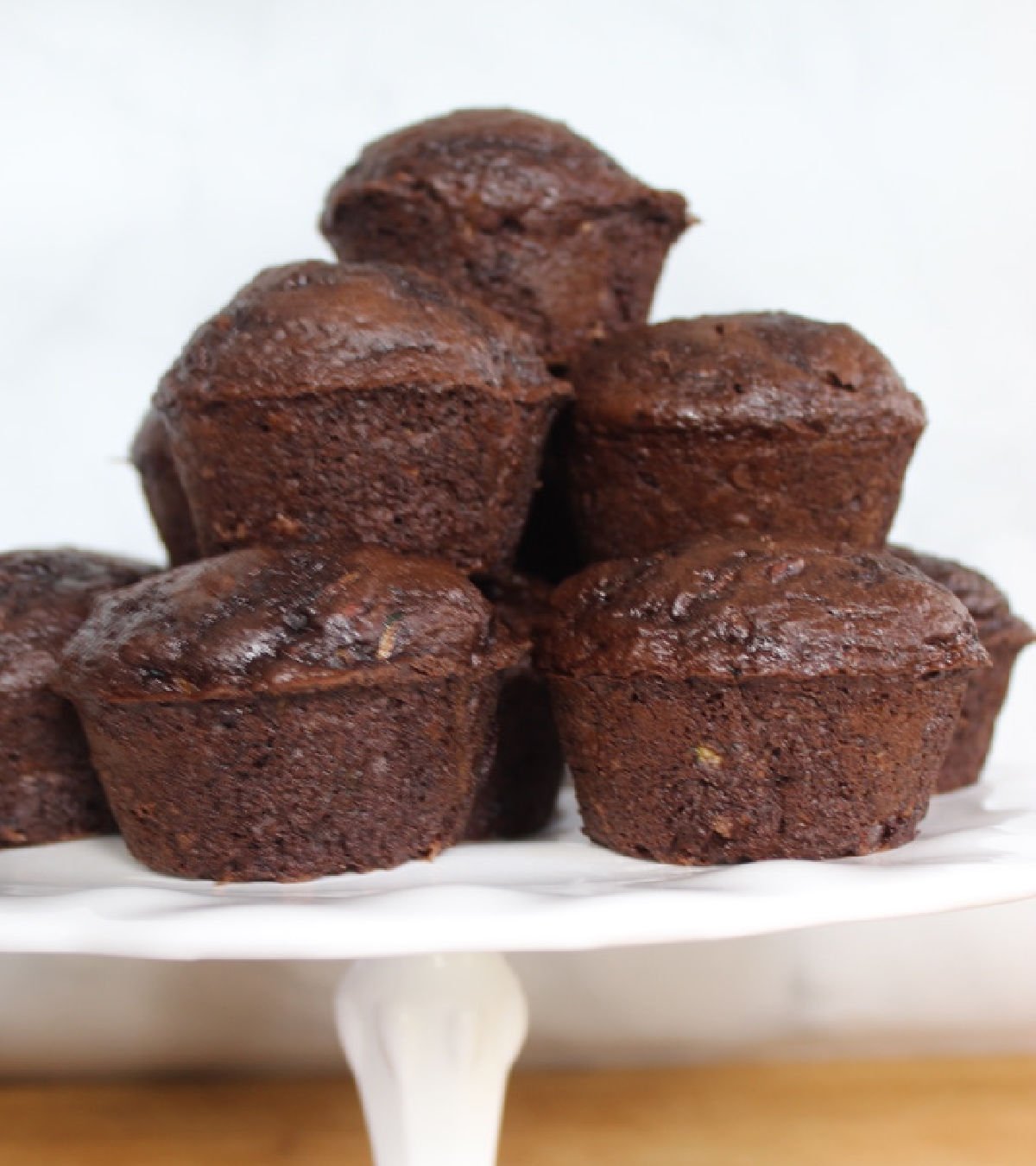 A white cake stand holding stacked chocolate zucchini muffins.