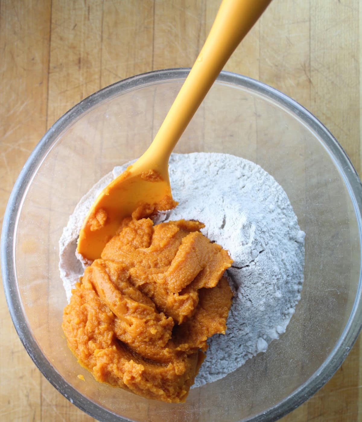orange pumpkin puree on a pile of cake mix in a clear glass bowl.