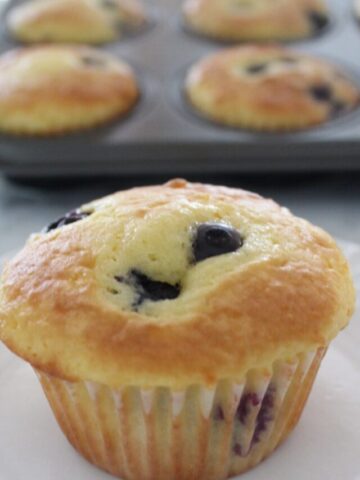 a blueberry muffin sitting in front of a muffin pan full of muffins