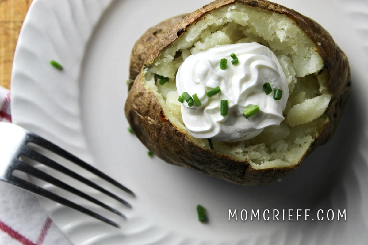 baked potato with sour cream and chives on a white plate