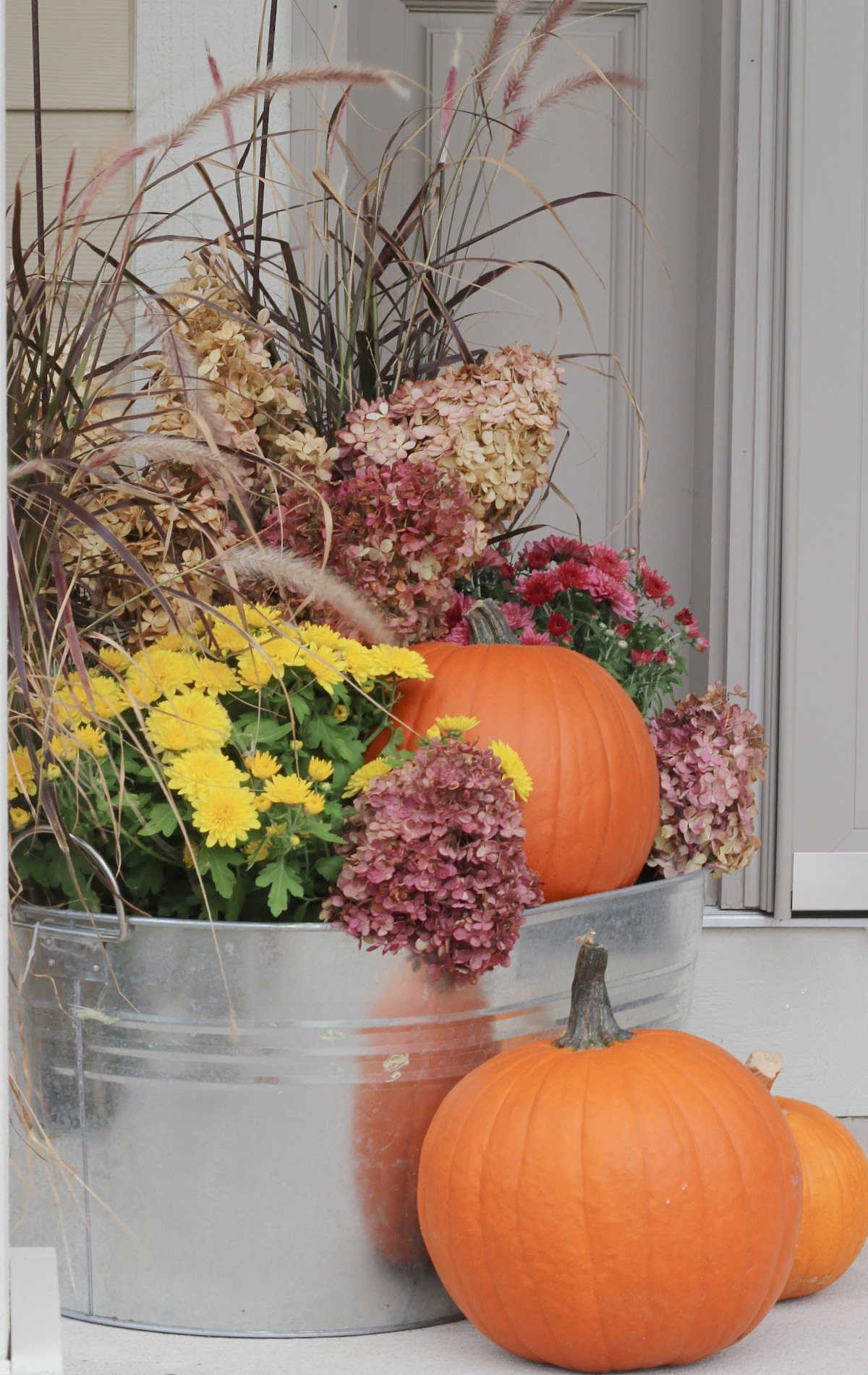 Colorful fall container arrangement with pumpkins, mums, and dried hydrangeas.
