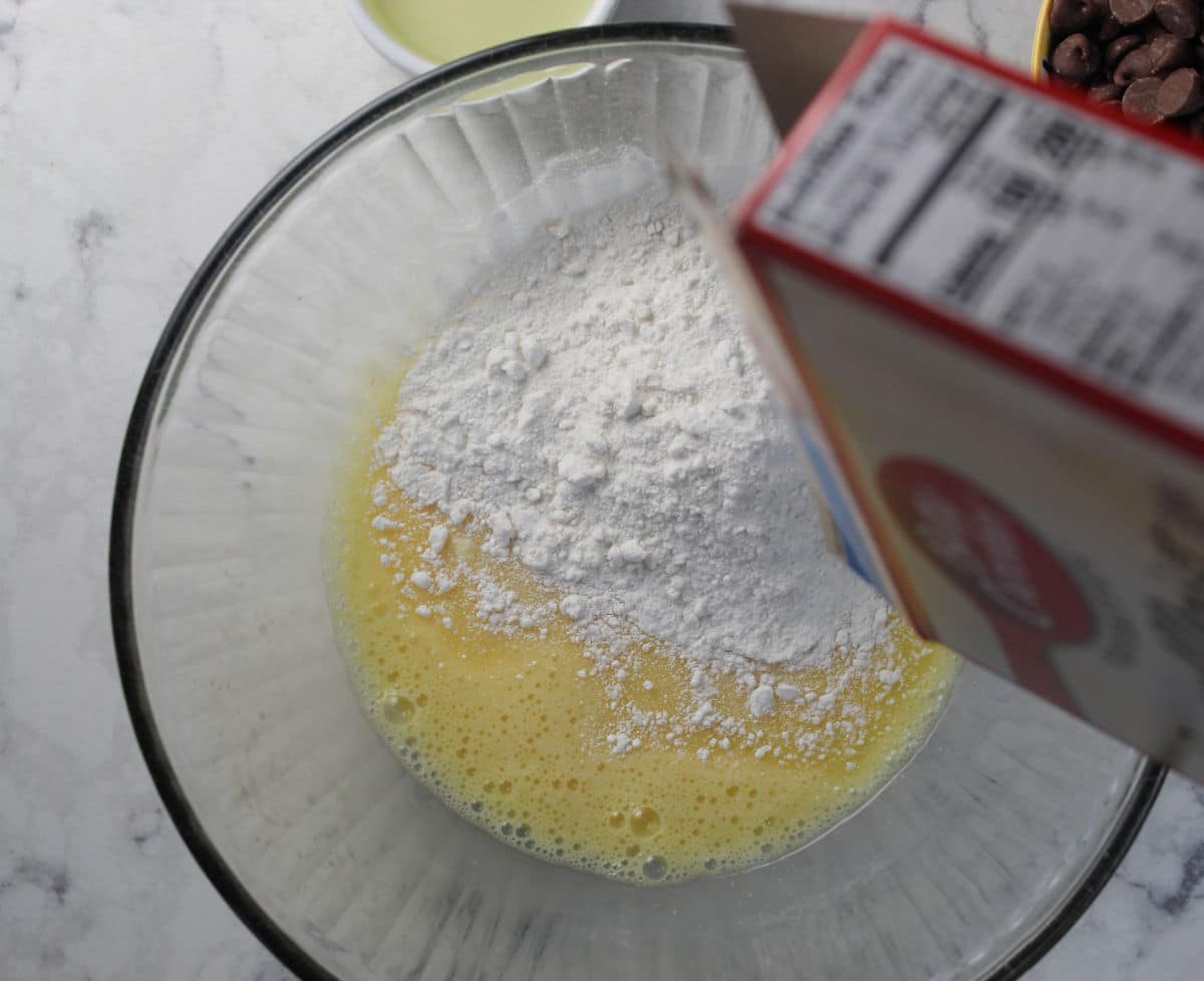 cake mix being added into egg and oil mixture of cookie bar dough.