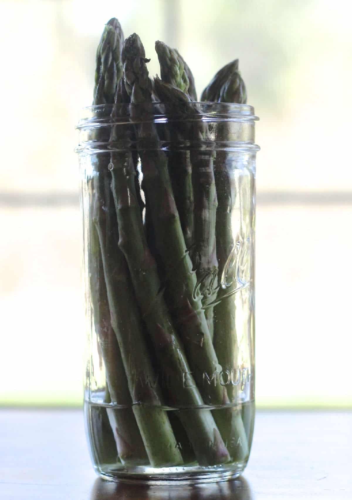 fresh asparagus in a mason jar with a little water in the bottom